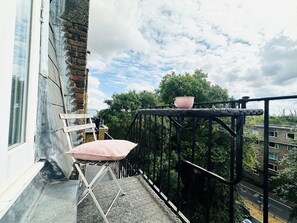 Een balkon met een metalen hekwerk, een opklapbare stoel en een roze kussen.