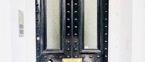 Eine schwarze Doppeltür mit einer Messingschild in der Mitte, eingelassen in eine weiße Wand.
