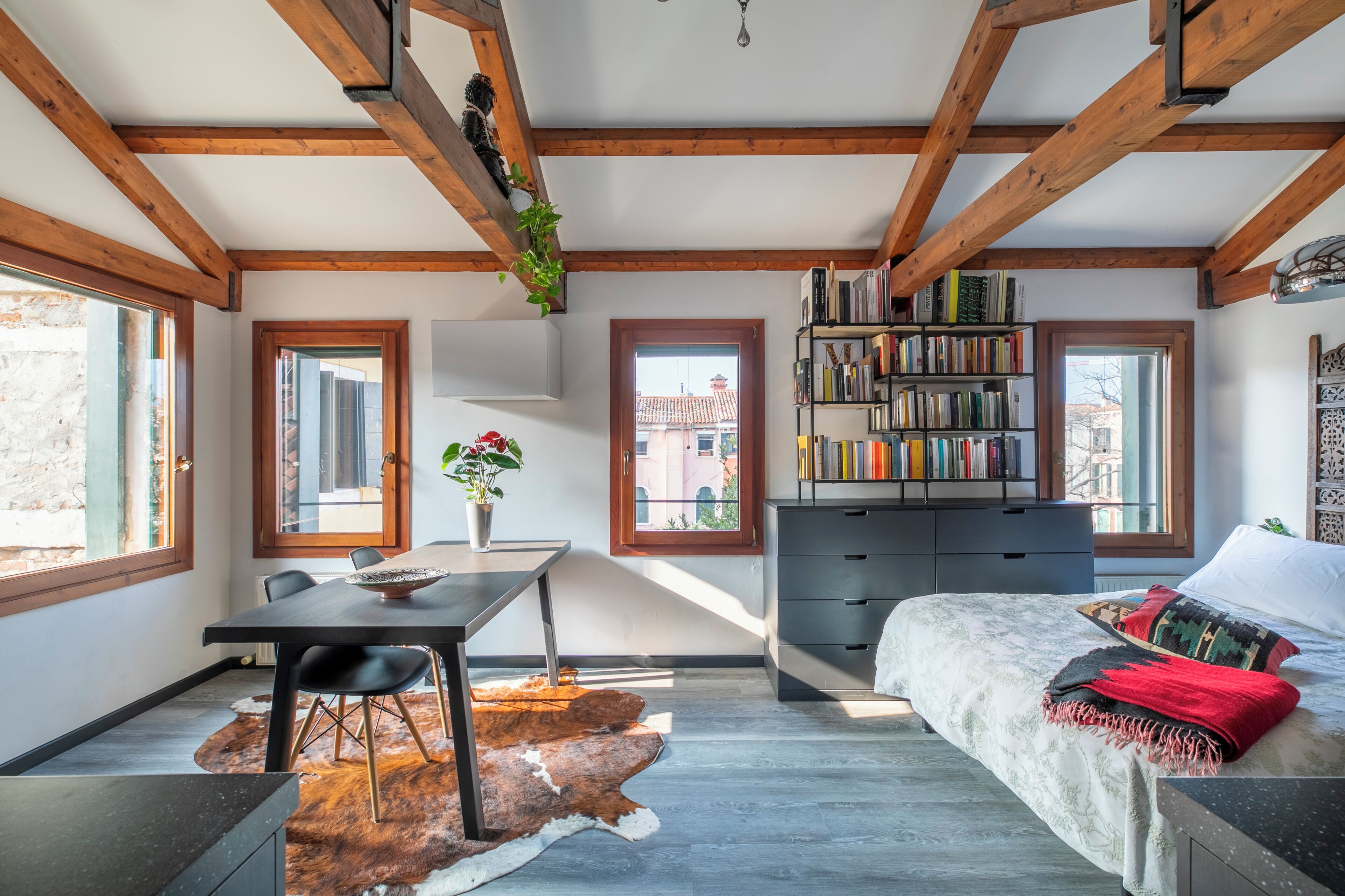 A compact room with a bed, a desk, a bookshelf, and a cowhide rug.