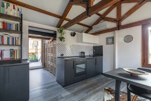 Une cuisine moderne avec des meubles de couleur sombre, un four encastré et un coin repas comprenant une table et des chaises.