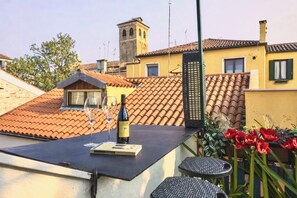 Une terrasse sur le toit avec une table, deux verres à vin et une bouteille de vin.