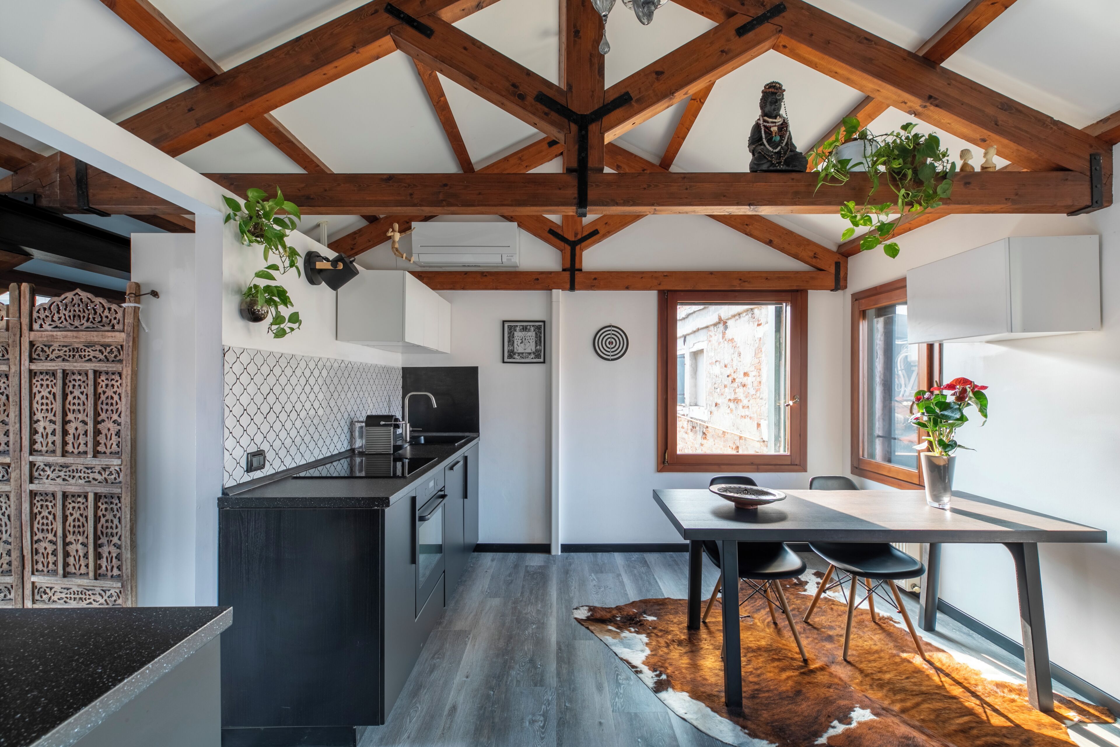 Une cuisine moderne avec un plafond en bois, un coin repas agrémenté d’un tapis en peau de vache, et une vue sur l’extérieur par une fenêtre.