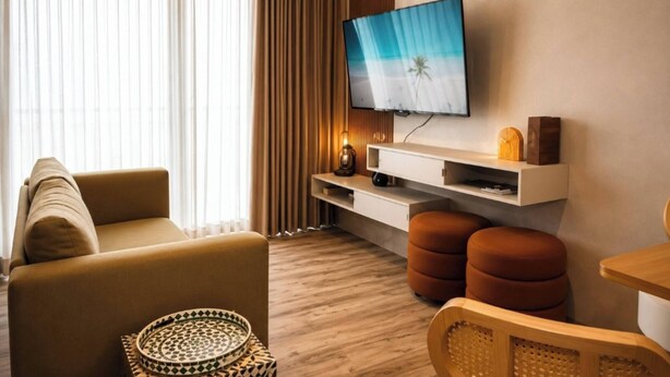 A modern living room with a sofa, ottomans, a flat-screen TV, and a wooden coffee table. - Seaside Escape at Luquillo Beach (Luquillo)