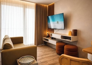 Ein modernes Wohnzimmer mit einer Couch, Hocker, einem Flachbildfernseher und einem Couchtisch aus Holz.