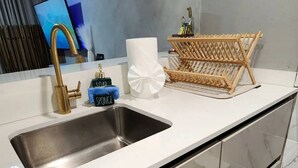 A modern kitchen with a stainless steel sink, a wooden drying rack, and a flat-screen TV mounted on the wall. - Seaside Escape at Luquillo Beach (Luquillo)