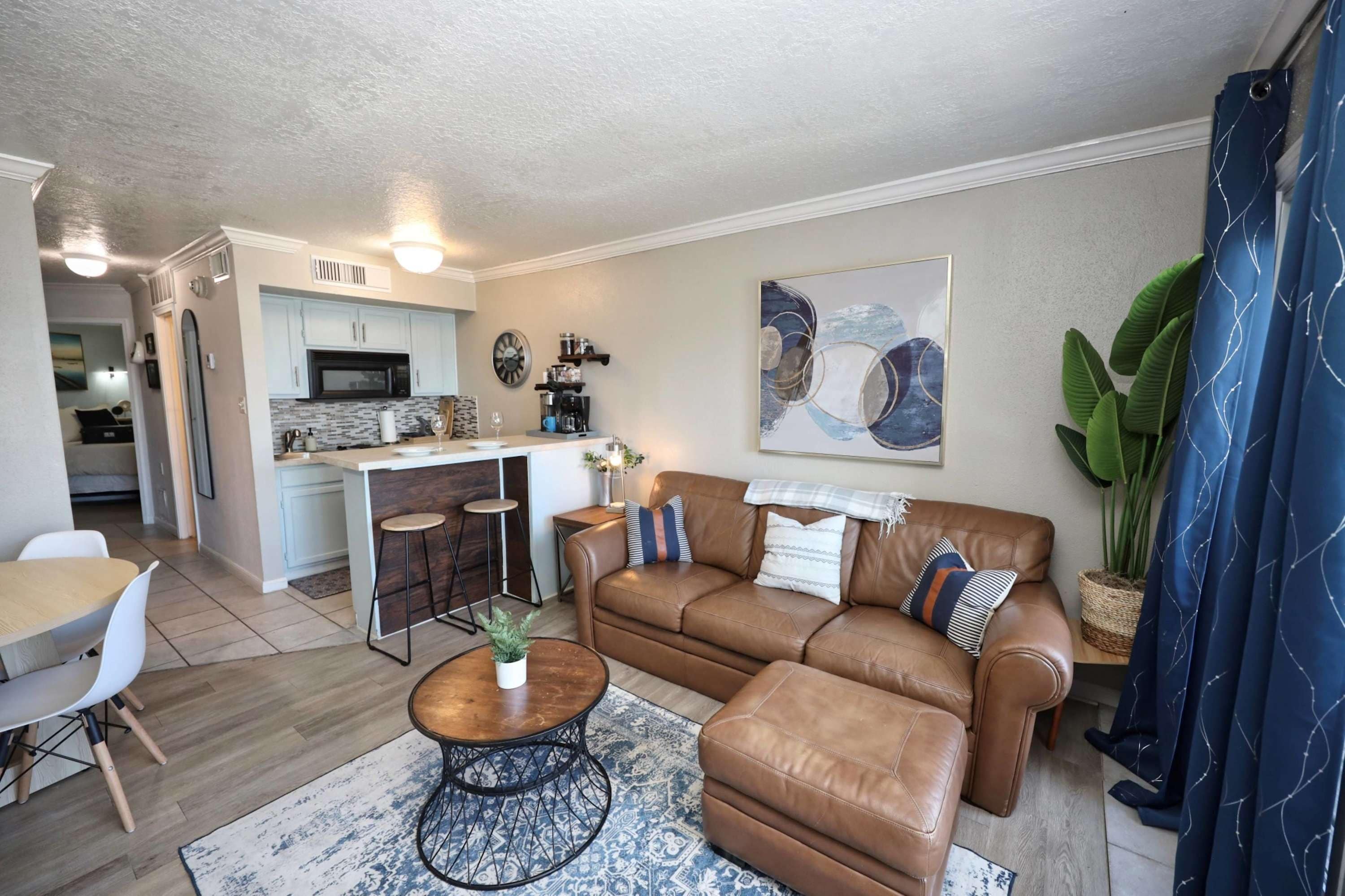 A modern living room with a brown leather sofa, a coffee table, and a dining area with a white table and chairs.