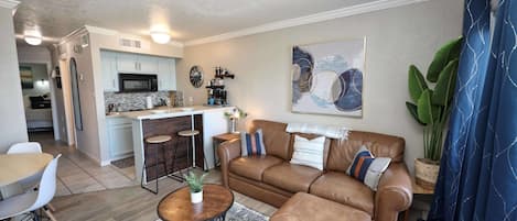 A modern living room with a brown leather sofa, a coffee table, and a dining area with a white table and chairs.