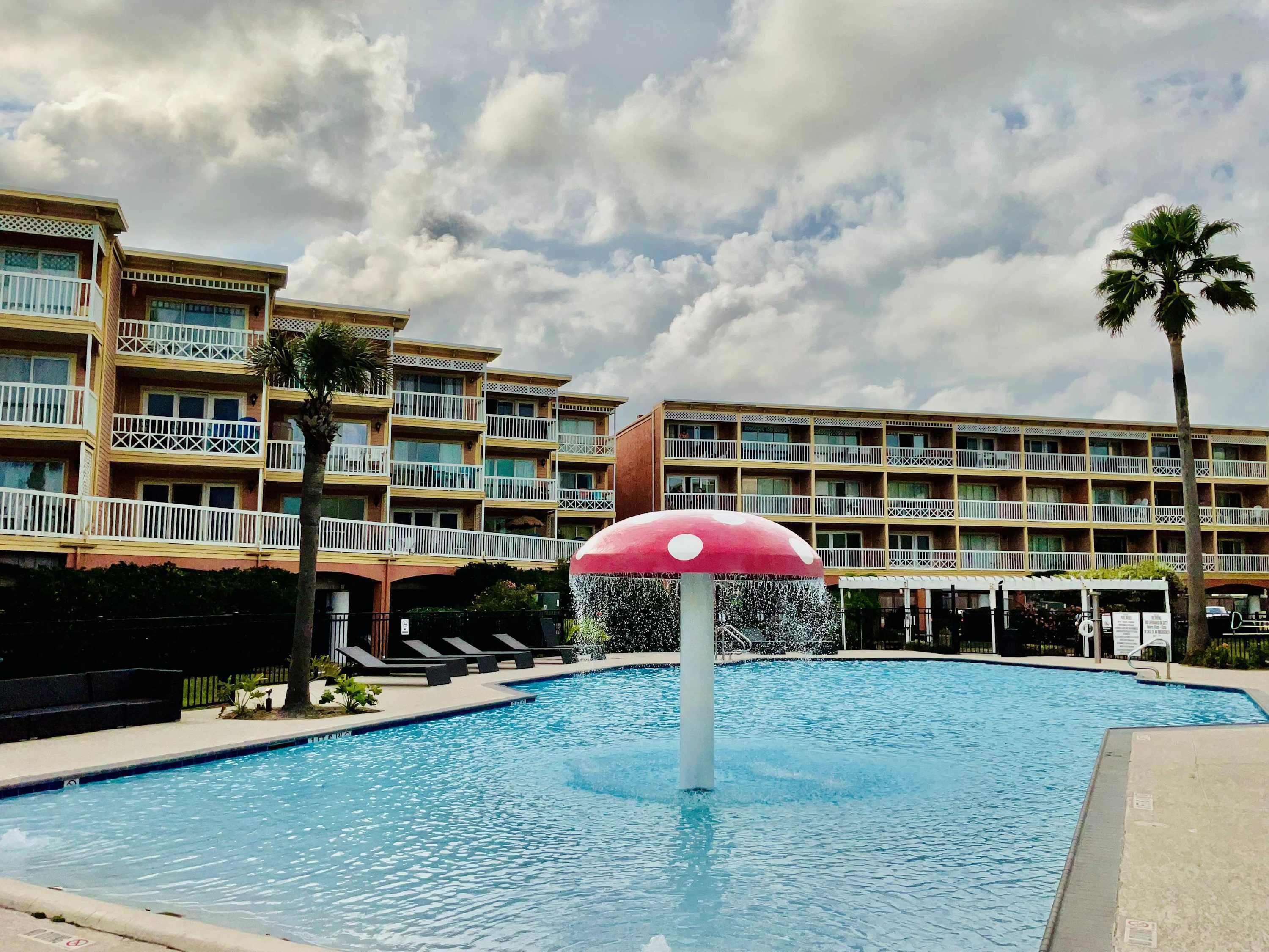 A swimming pool with a water fountain, surrounded by multi-story buildings with balconies.