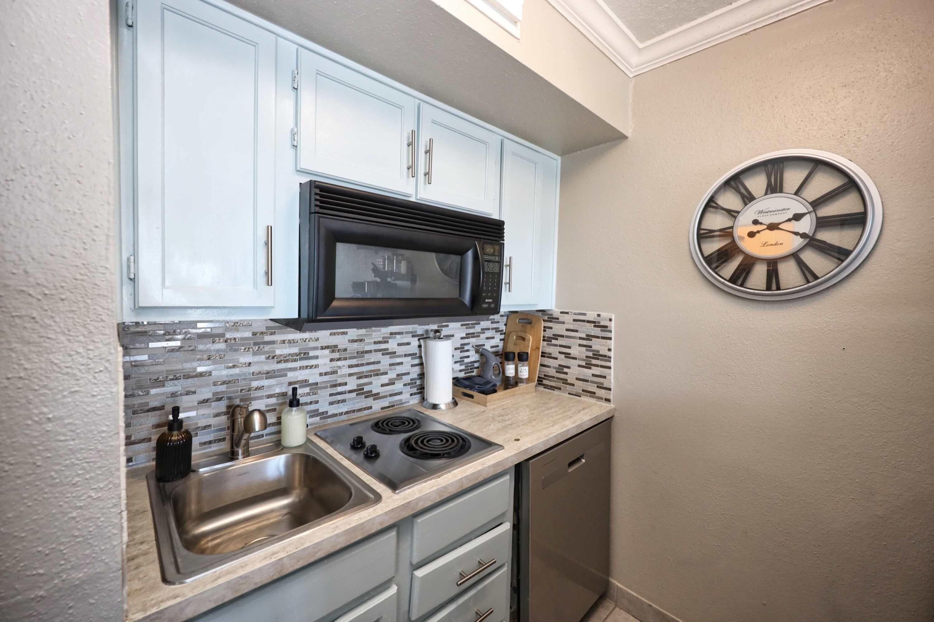 A compact kitchen with a microwave, stove, sink, and a clock on the wall.