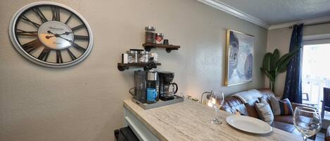 A kitchen with a large wall clock, coffee maker, and shelves with jars.