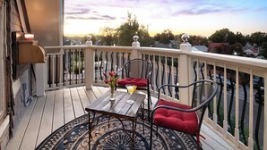 A balcony with a table and chairs, a view of the neighborhood, and a sunset in the background.