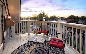 A balcony with a table and chairs, a view of the neighborhood, and a sunset in the background.