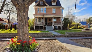 A two-story house with a front porch, a flagpole, and a garden with red and yellow flowers.