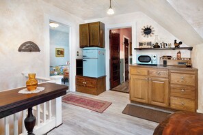 Une cuisine avec des meubles de rangement en bois, un réfrigérateur ancien, un four à micro-ondes et une horloge au mur.