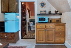 Une cuisine avec un réfrigérateur bleu, un four à micro-ondes, des armoires en bois et une horloge au mur.