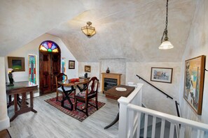 A dining area with a wooden table and chairs, a stained glass window, and a fireplace.