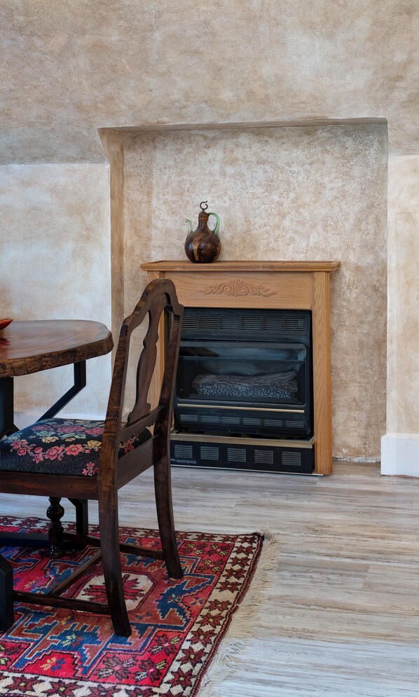 A room with a fireplace, a wooden chair, a table, and a patterned rug.