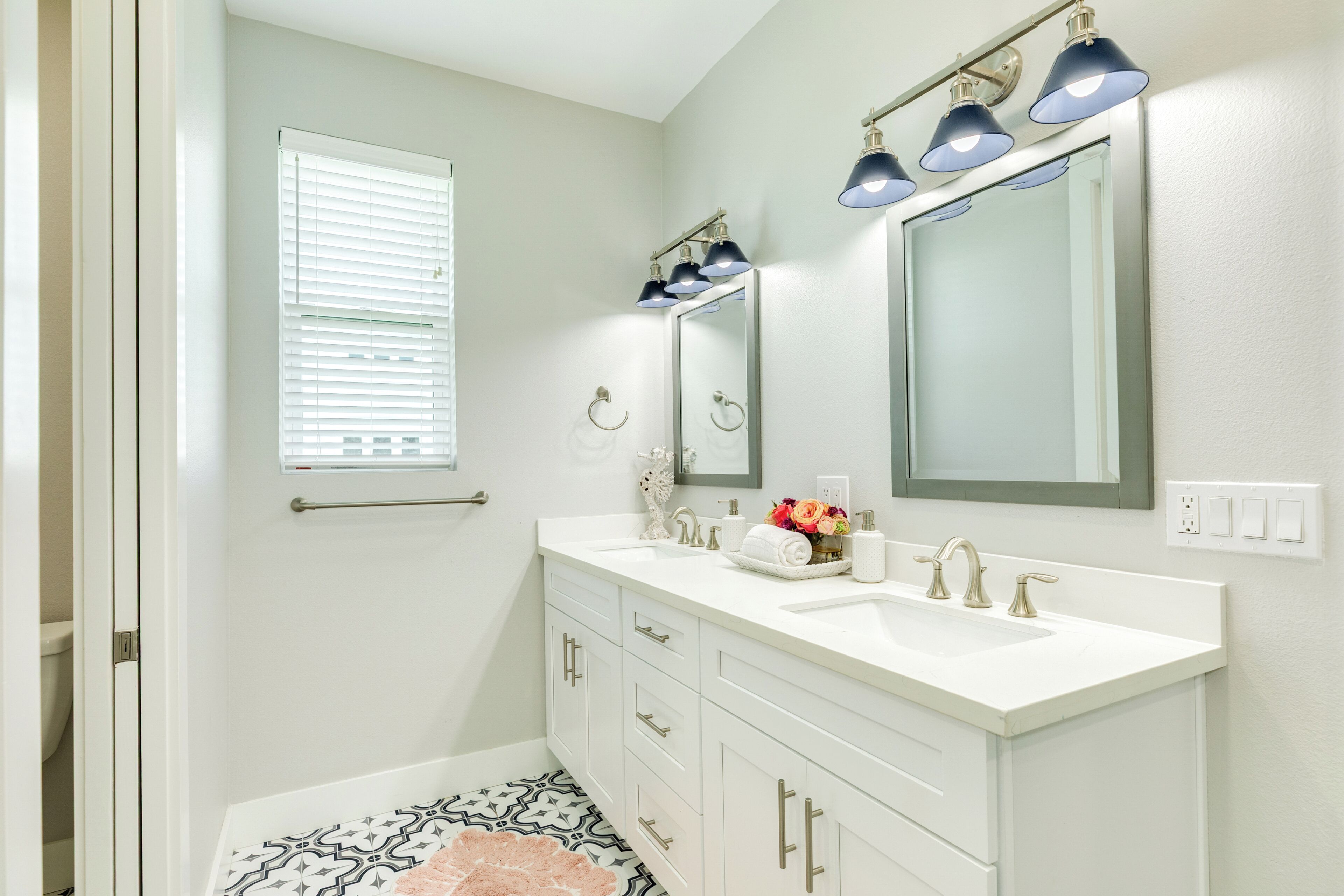 A bathroom with a white vanity, a large mirror, and a window with blinds.