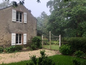 Ein rustikales Steinhaus mit weißen Fensterläden, einer Schotterauffahrt und einem Drahtzaun.