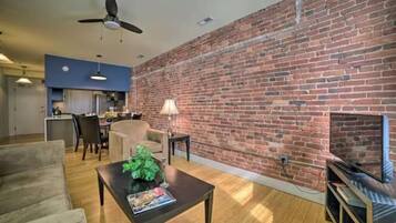 A living room with a brick wall, a ceiling fan, a fireplace, and a television.