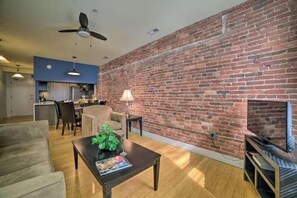 A living room with a brick wall, a ceiling fan, a fireplace, and a television.