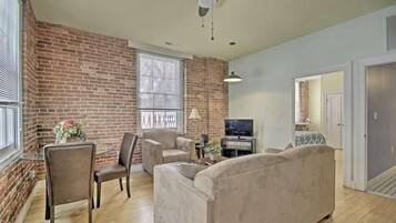 A living room with a brick wall, a ceiling fan, a TV, and a sofa.