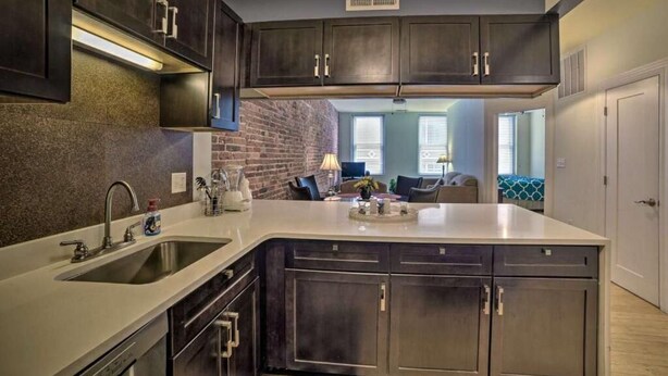 A modern kitchen with dark cabinetry, a large island, and a brick accent wall.