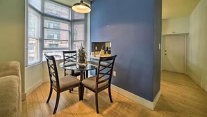 A dining area with a round table, four chairs, a hanging light fixture, and large windows. - Convention center Indoor free parking (Baltimore)