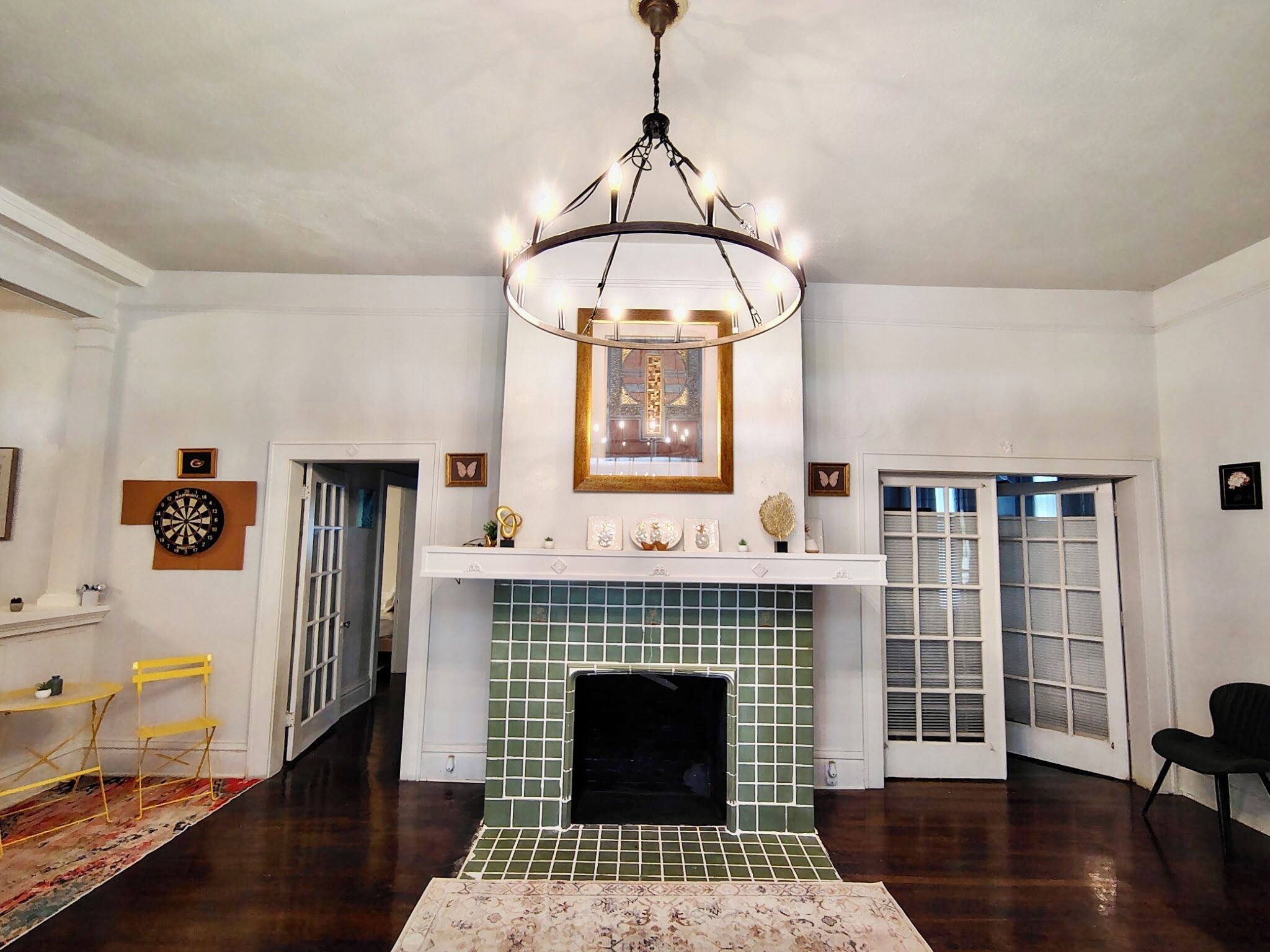 A room with a fireplace, a chandelier, a dartboard, and a door leading to another room.
