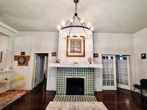 Una habitación con chimenea, candelabro, dardo y puerta que da a otra estancia.