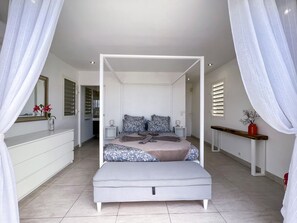 A bedroom with a canopy bed, bedside tables, a dresser, and a mirror. - Villa Panorama Marin · Bois Jolan · 5 BR · 426969 (Sainte-Anne)