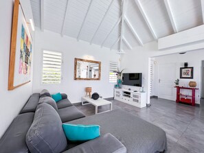 A modern living room with a grey sofa, a white entertainment unit, and a large mirror. - Villa Panorama Marin · Bois Jolan · 5 BR · 426969 (Sainte-Anne)