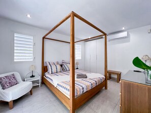 A bedroom with a four-poster bed, a bedside table, a chair, a desk, and a potted plant. - Villa Panorama Marin · Bois Jolan · 5 BR · 426969 (Sainte-Anne)