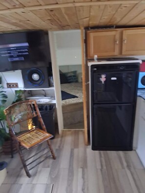 A compact kitchen with a black refrigerator, a wooden cabinet, and a chair.