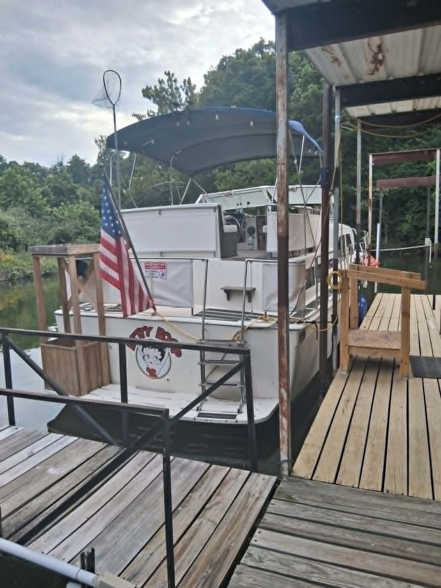 Ein Boot liegt an einem hölzernen Steg, mit einer amerikanischen Flagge, einem überdachten Bereich und einem kleinen Tisch.