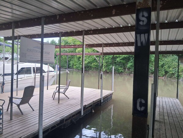 A covered dock with a chair and a sign, surrounded by water and greenery.