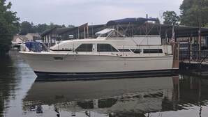 A white boat docked at a marina with a covered area and a flag.