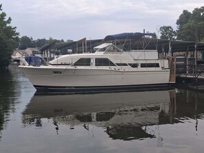 A white boat docked at a marina with a covered area and a flag.