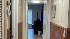 A hallway with a ceiling light, wooden paneling, a trash can, and a door leading to a room. - Beautiful condo ocean view. (New Smyrna Beach)