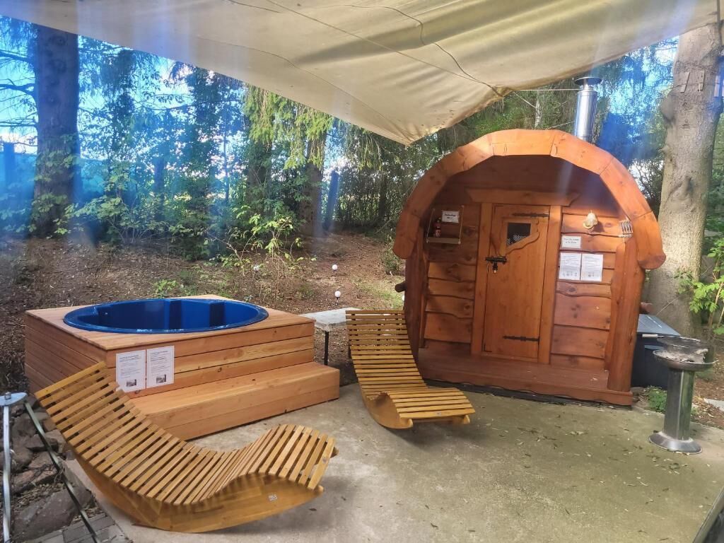 Un jacuzzi de madera y un área de sauna con entrada cubierta, rodeado de árboles.