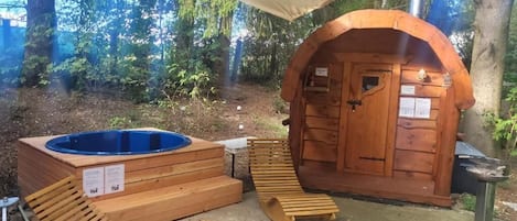 A wooden hot tub and a sauna area with a covered entrance, surrounded by trees.