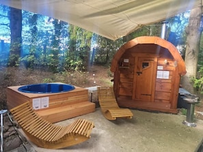 A wooden hot tub and a sauna area with a covered entrance, surrounded by trees.