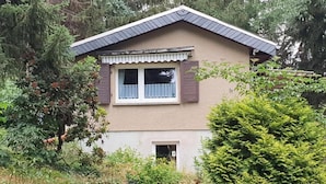 Una casa de dos pisos con techo a dos aguas, un pequeño porche y una ventana con contraventanas.
