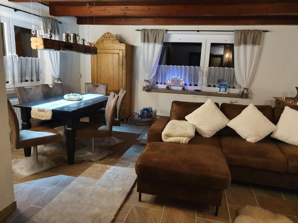 A cozy living room with a brown sofa, a dining table with chairs, and a window with curtains.