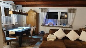 A cozy living room with a brown sofa, a dining table with chairs, and a window with curtains.