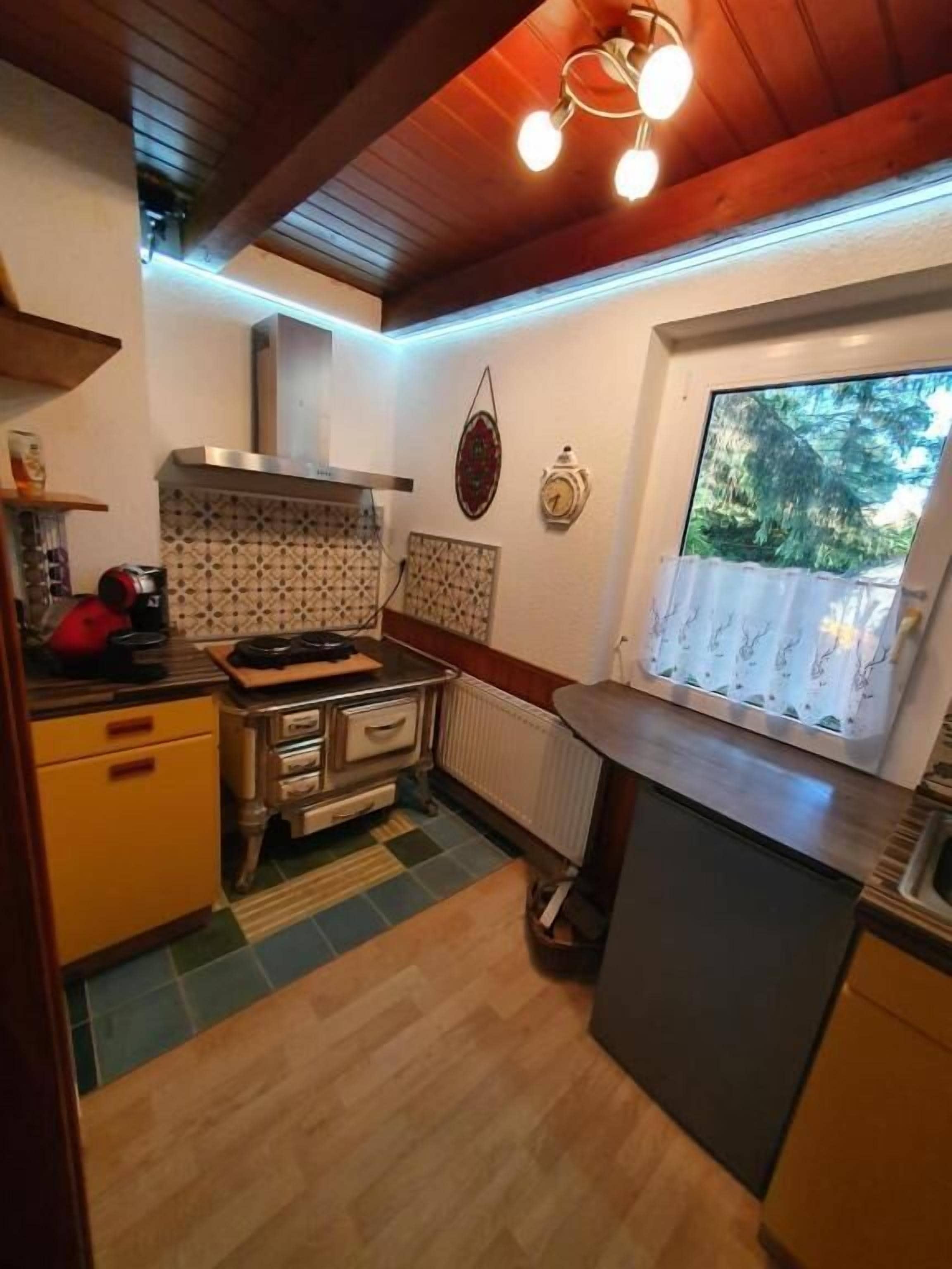 A compact kitchen with a wooden ceiling, a window with a view of greenery, and a tiled backsplash.