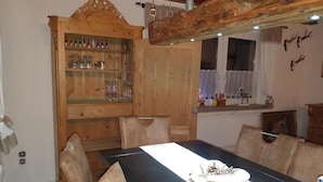 Un comedor con una mesa larga, sillas de madera, un aparador con cristalería y un techo rústico.