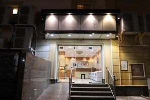 Entrada de hotel con una escalera que sube, un mostrador de recepción y una puerta de cristal.