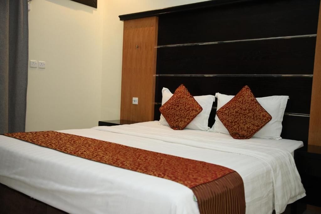A hotel room with a bed, a wooden headboard, and a patterned throw blanket.