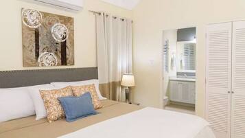 Quarto de hotel com cama, mesa de cabeceira, luminária, banheiro com espelho e guarda-roupa.